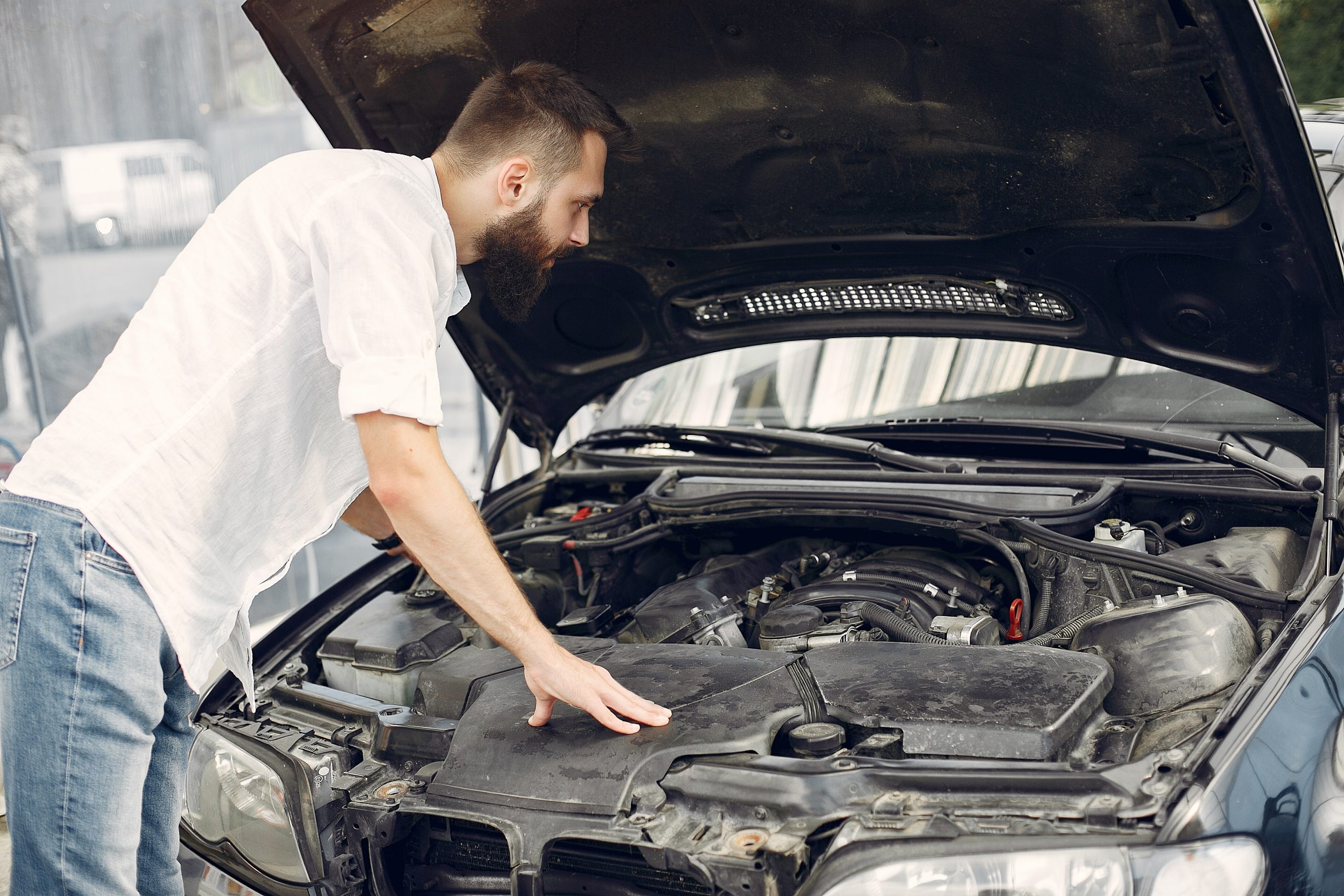 Man checks the engine. Guy checks his car Male in a white shirt.